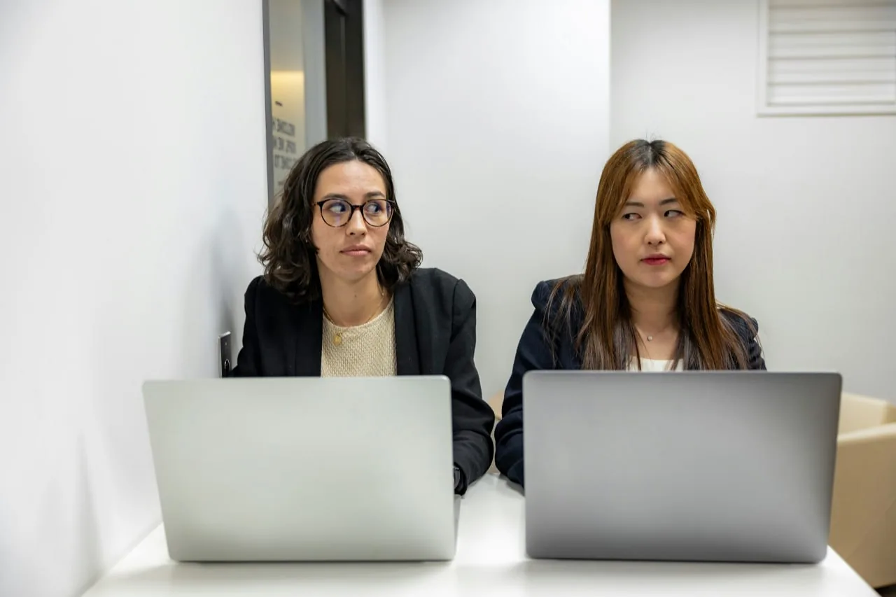 Two women working on laptops together in an office, suggesting a small business advertising agency team at work