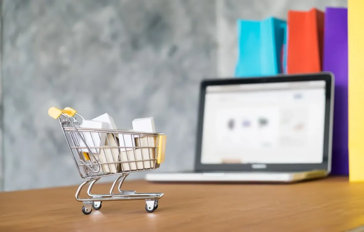 Mini shopping cart on a desk in front of a laptop, suggesting online campaign management and digital purchasing workflows Mini shopping cart on a desk in front of a laptop, suggesting online campaign management and digital purchasing workflows