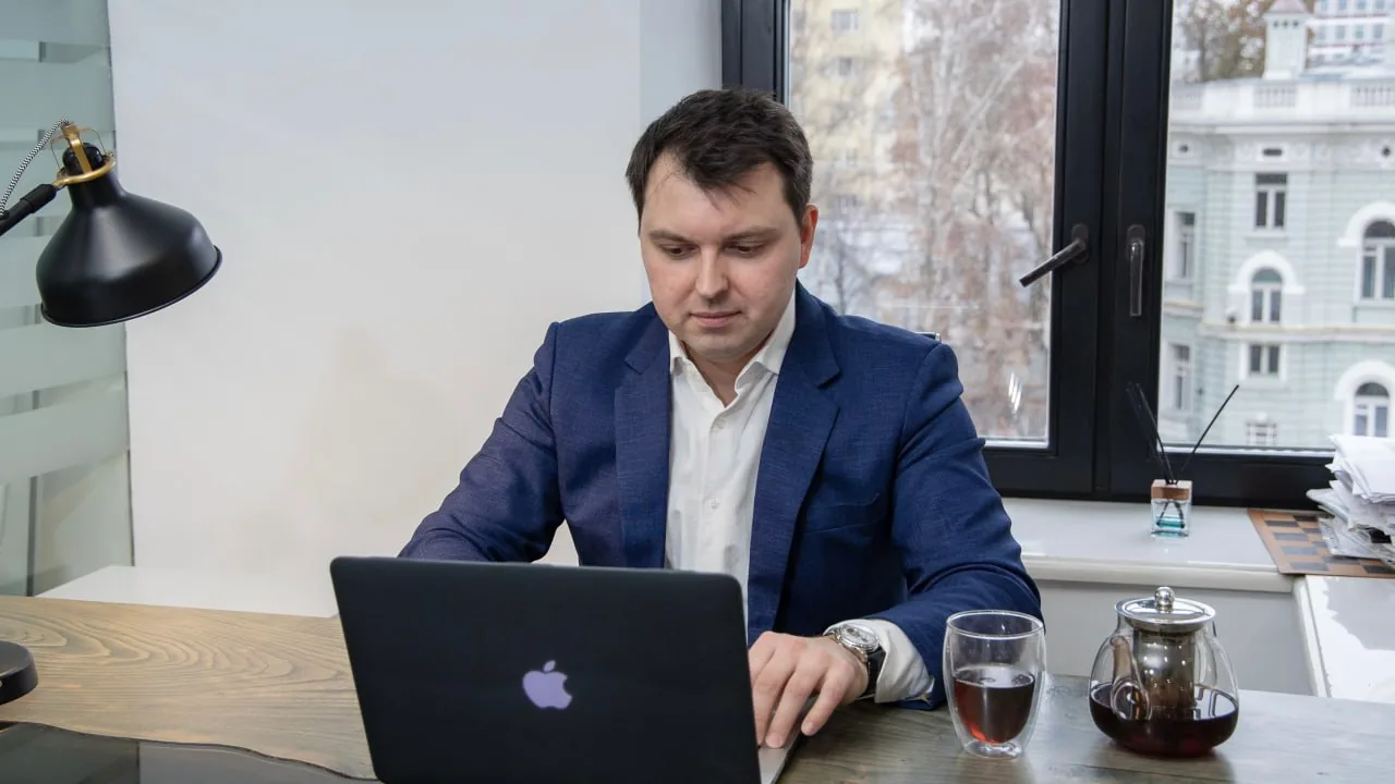 Man in a blue blazer working on a laptop at an office desk with tea nearby