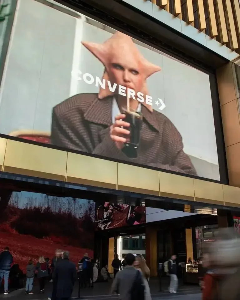Large city billboard advertising a drink above people walking on a sidewalk, representing public-facing creative advertising work Large city billboard advertising a drink above people walking on a sidewalk, representing public-facing creative advertising work