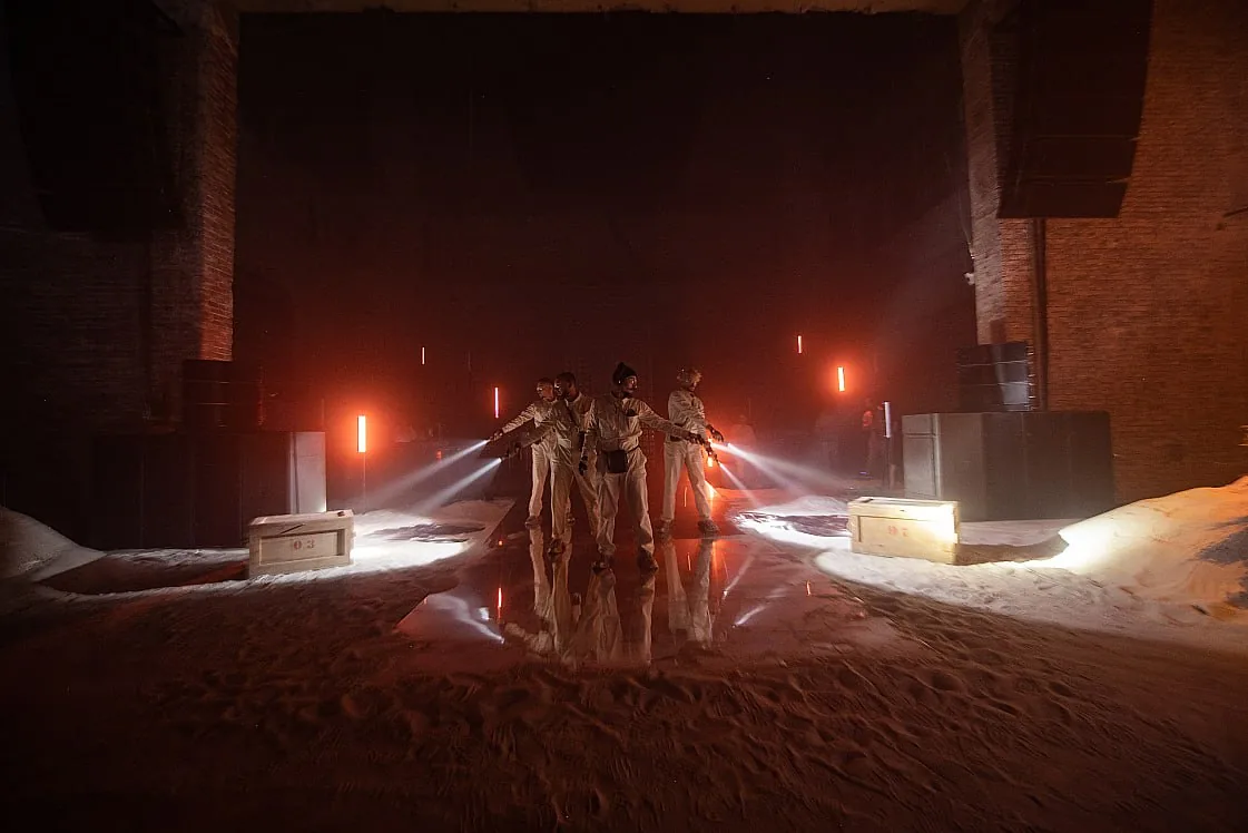 Team in light suits standing together in an industrial setting with red stage lighting and smoke