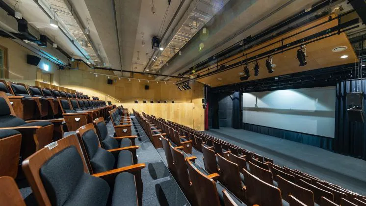Empty auditorium with rows of seats facing a stage and large screen, suggesting preparation for a presentation or launch event